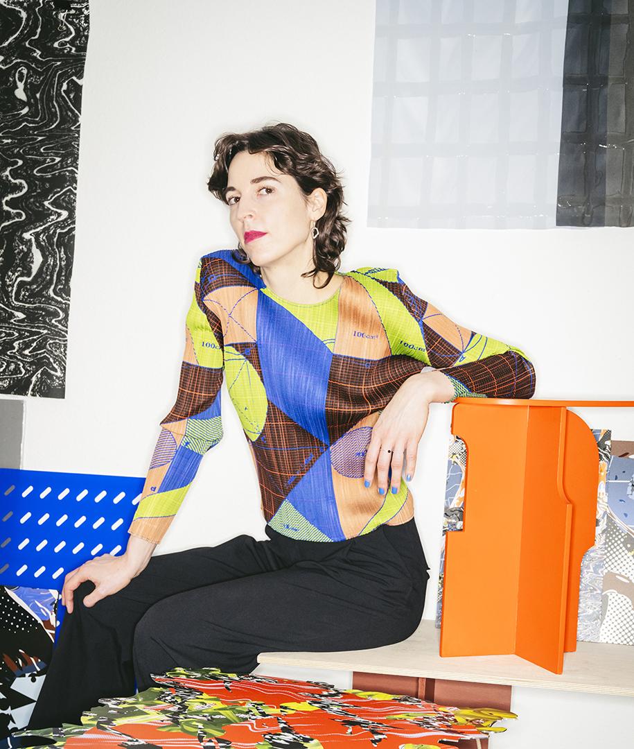 The Designer Anna Resei in a colorful blouse, sitting in her studio among her works
